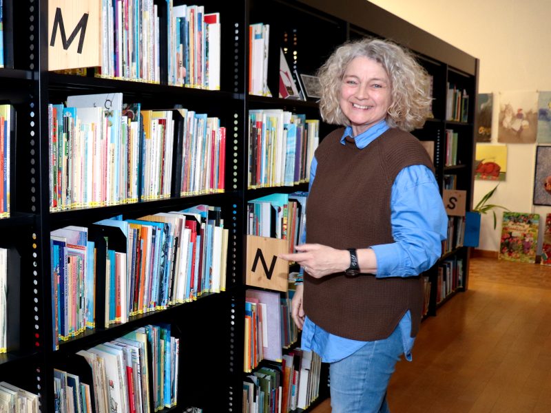 Leslie Schnyder steht in der Bibliothek des PMZ vor der Bilderbuchsammlung.