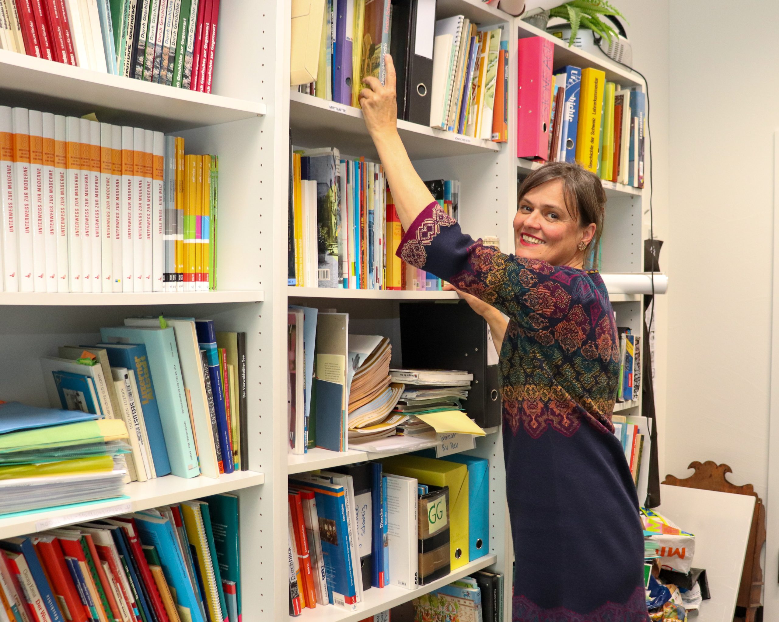 Sabine Ziegler, Dozentin für Geschichtsdidaktik steht in ihrem Büro vor dem Bücherregal und sucht ein Buch aus.