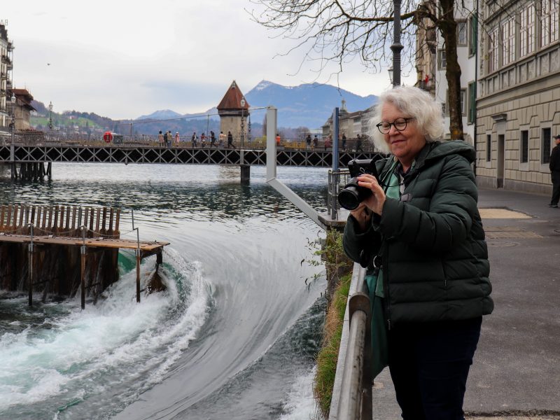 Heidi Wüthrich steht mit einer Fotokamera an der Reuss. Es ist ihr Lieblingsort an der Reuss, weil dort das Wasser so schön schäumt.